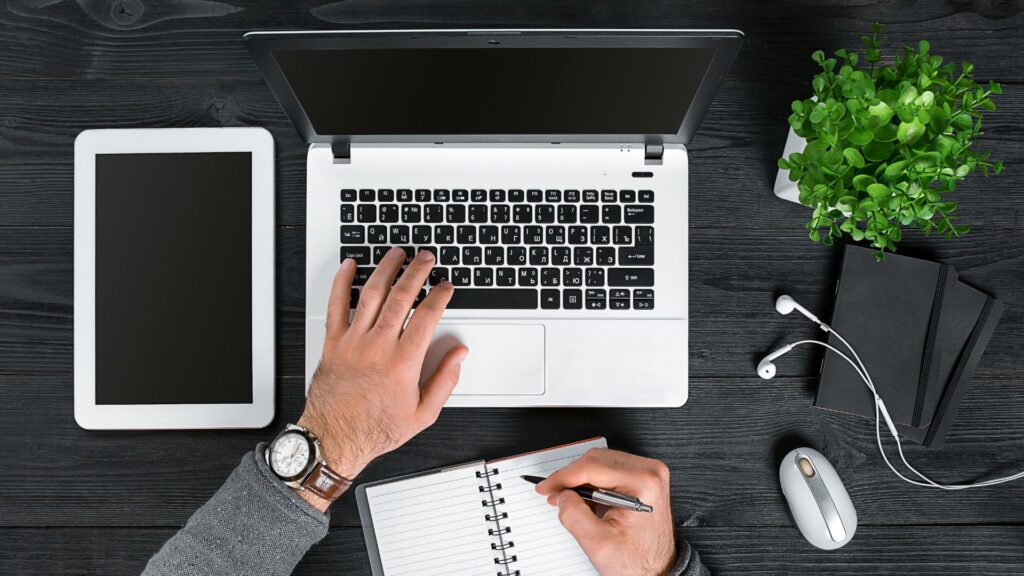 Escritorio de profesionista trabajando en una laptop con tablet al lado y libreta de anotaciones